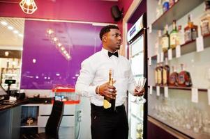 African american bartender at bar holding champagne with glasses. photo