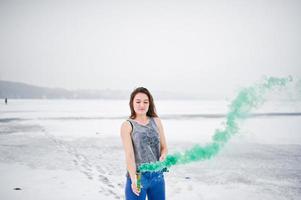 niña con bomba de humo de color verde en la mano en el día de invierno. foto