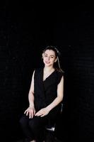 Portrait of a beautiful brunette girl in black jumpsuit sitting and posing in the studio. photo