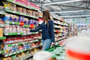 mujer de compras mirando los estantes del supermercado. retrato de una joven en una tienda de mercado con una cesta verde. foto