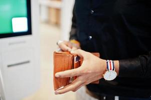 Hands of man customer at store place orders and pay through self pay floor kiosk for fast food, payment terminal. His holding wallet and find credit card. photo