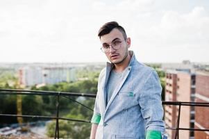 Dreamer stylish macho man in gray suit and glasses posed on the roof. photo