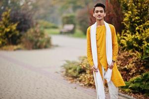 Indian stylish man in yellow traditional clothes with white scarf posed outdoor. photo