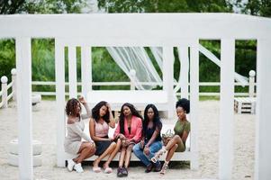 Group of five african american girls relaxing at beautiful poolside cabana beside luxury resort. photo