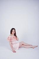 Portrait of a fashionable woman in pink dress sitting and posing on the floor in the studio. photo