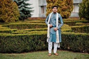 Indian man wear on traditional clothes with white scarf posed outdoor against green bushes at park. photo