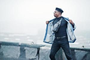 hombre afroamericano con chaqueta de jeans, boina y anteojos posados en un techo abandonado. foto