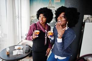 Two curly hair african american woman wear on sweaters with cups of tea posed at cafe indoor. photo