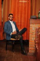 Handsome well-dressed arabian man with glass of whiskey and cigar posed at pub. photo