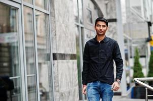 Stylish indian model man in casual clothes, black shirt posed outdoor at street of India. photo