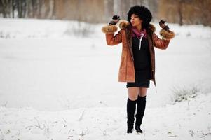 mujer afroamericana de pelo rizado con abrigo de piel de oveja y guantes posados en el día de invierno. foto