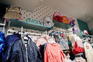 la ropa brillante de los niños cuelga en la pantalla de la tienda de ropa para bebés. sección de chicas. foto