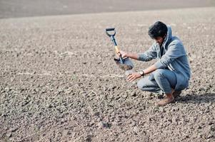 South asian agronomist farmer with shovel inspecting black soil. Agriculture production concept. photo