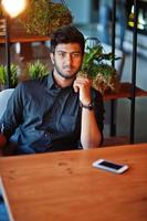 Confident young indian man in black shirt sitting at cafe. photo