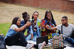 Group of five african college students spending time together on campus at university yard. Black afro friends making with mobile phones. Education theme. photo