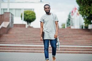 African student male posed with backpack and school items on yard of university, against flags of different countries. photo