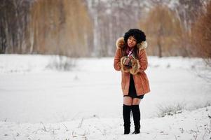 El cabello rizado de una mujer afroamericana con abrigo de piel de oveja y guantes posados en el día de invierno muestra que hace frío. foto