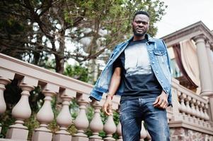 Young attractive serious african american man model. Modern handsome guy in jeans jacket standing on urban city street. photo