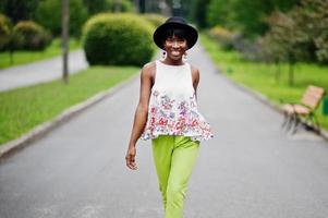 Amazing african american model woman in green pants and black hat posed with different emotions at park. photo
