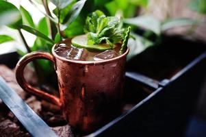 Alcoholic cocktail with ice, mint and lime in bronze cup on bar table. photo