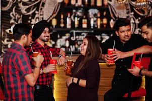 Group of indian friends having fun and rest at night club, drinking cocktails near bar counter. photo