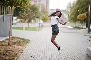 African american dark skinned slim model posed in a black leather shorts and white t-shirt. She jumping at the air. photo