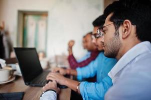 Group of four south asian men's posed at business meeting in cafe. Indians work with laptops together using various gadgets, having conversation. photo
