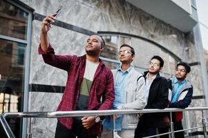 Group of four indian teen male students. Classmates spend time and make selfie by phone together. photo