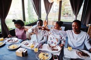 Happy african friends sitting, chatting in cafe and eat food. Group of black peoples meeting in restaurant and have dinner. Gives high five each other. photo