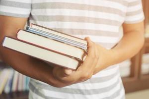 close up student young man hand holding books are placed front bookshelf in a library University. love to read education concept. with filter Tones retro vintage warm effect. photo