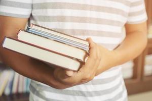 close up student young man hand holding books are placed front bookshelf in a library University. love to read education concept. with filter Tones retro vintage warm effect. photo