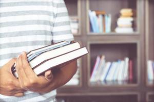 primer plano estudiante joven mano sujetando libros se colocan estantería frontal en una biblioteca universitaria. Me encanta leer el concepto de educación. con tonos de filtro efecto cálido vintage retro. foto