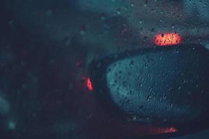 gotas de lluvia lloviznan en el parabrisas de cristal por la noche. calle bajo la fuerte lluvia. Bokeh luz trasera y semáforos en la ciudad. conduzca el automóvil con cuidado, camino resbaladizo. enfoque suave. foto