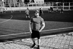 Young brutal bearded muscular man wear on red shirt, shorts and cap at stadium. photo