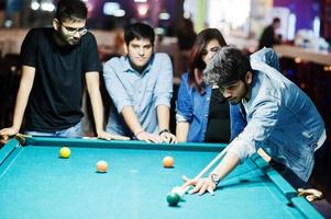 Group of stylish asian friends wear on jeans playing pool billiard on bar. photo