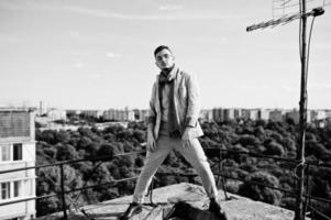 Dreamer stylish macho man in gray suit, scarf and glasses posed on the roof. photo