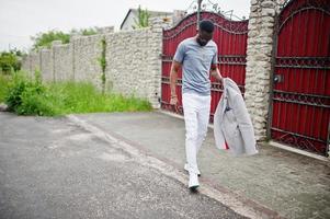 Rich and stylish african american man in blazer and eyeglasses outdoor against red fence. photo