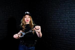 FBI female agent in cap and with gun at studio against dark brick wall. photo