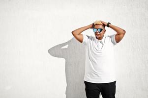 Stylish arabian muslim boy with originally hair and sunglasses posed on streets at roof against white wall. photo