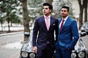 Two elegant indian fashionable mans model on suit posed at winter day against black classic car. photo