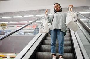 African woman with shopping eco bags on escalator at mall. photo
