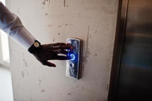 foto de primer plano de la mano del hombre afroamericano con relojes en elavator o ascensor moderno, presionando el botón.