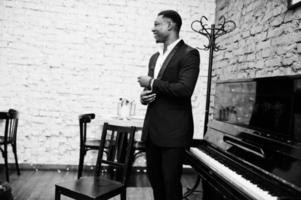 Strong powerful african american man in black suit standing against piano. photo