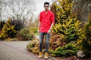 hombre indio con camisa roja y gafas de sol posó al aire libre. foto