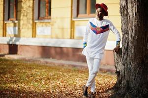 Stylish trendy afro france man in red hat and white outfit posed at autumn day. Black african model guy. photo