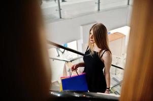 chica con bolsas de compras en el centro comercial en la escalera mecánica. foto