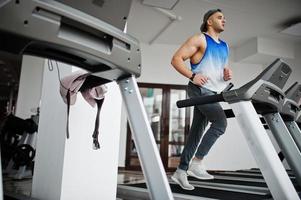 Fit and muscular arabian man running on treadmill in gym. photo