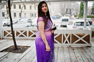 Indian hindu girl at traditional violet saree posed at street against wooden terrace. photo