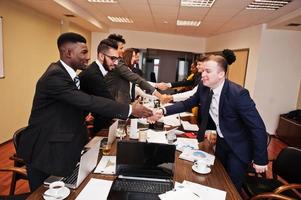 buen negocio. equipo de negocios multirracial que se dirige a la reunión alrededor de la mesa de juntas y se da la mano. foto