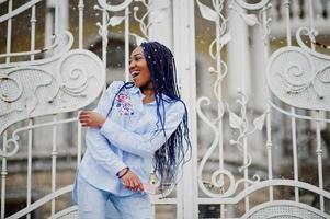 Stylish african american girl with dreads holding mobile phone at hand, outdoor against white royal gates at snowy weather. photo